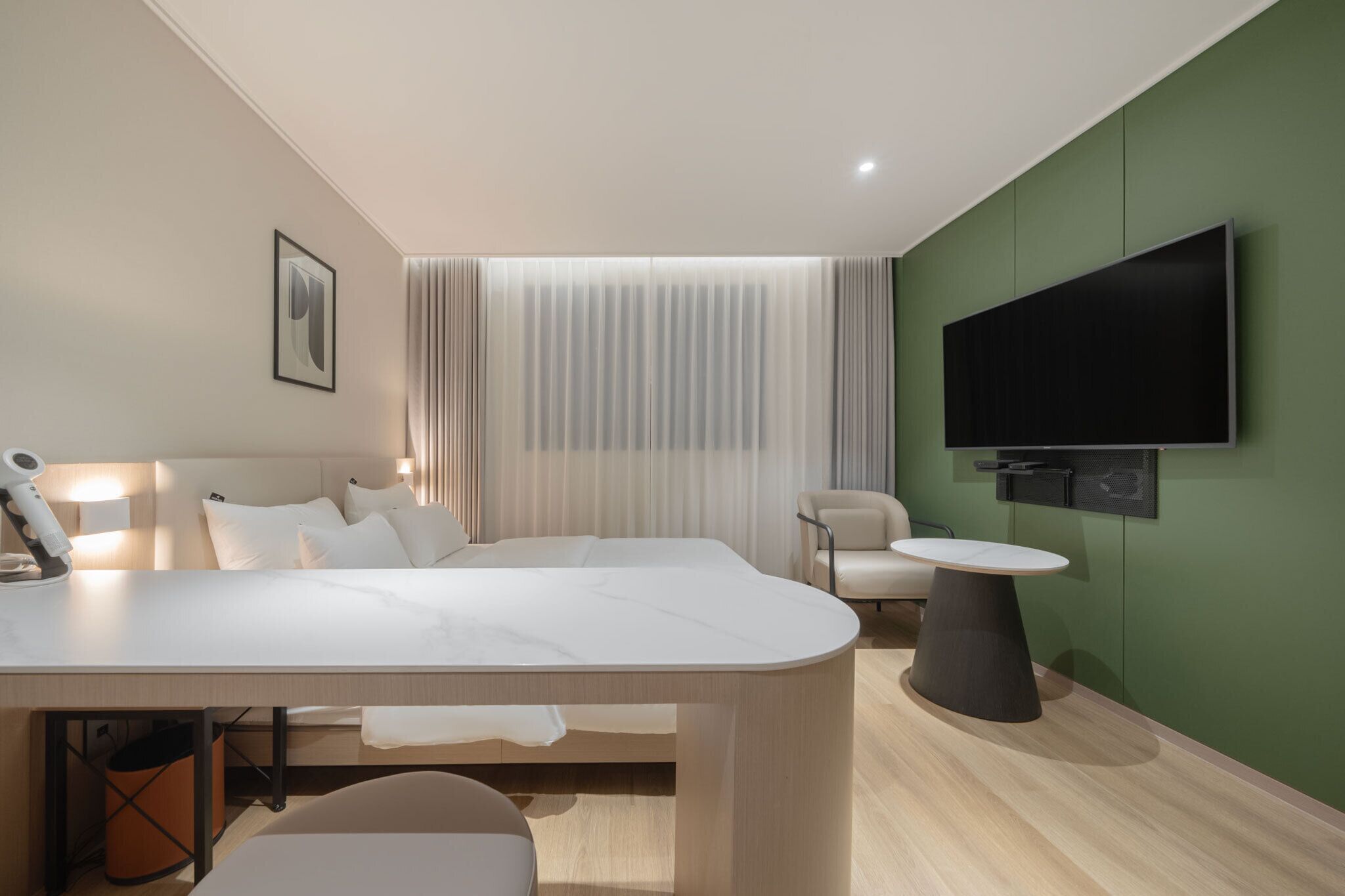 Quarto de hotel moderno com uma cama grande, uma escrivaninha, uma TV de tela plana e uma parede verde decorativa.