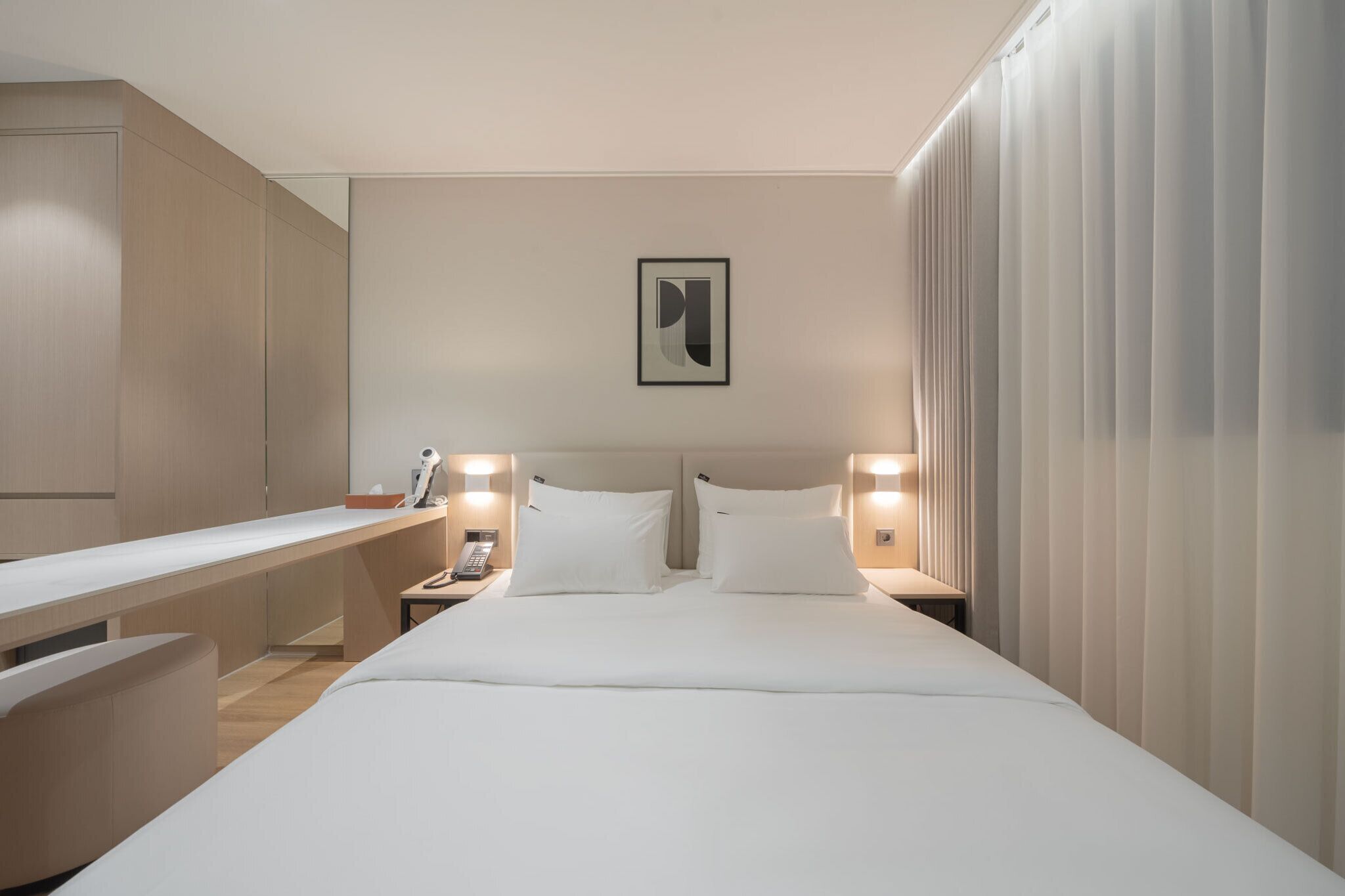 A hotel room with a bed, bedside tables, a desk, and a large window with curtains.