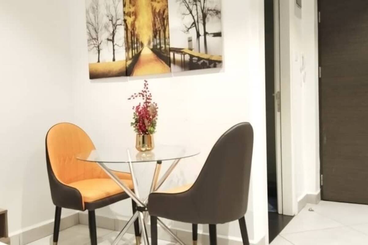 A modern room with a glass table and two chairs, one orange and one black.