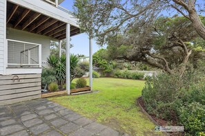 Enjoy a serene garden setting with a wooden deck and covered porch, surrounded by mature trees and a secure fence.