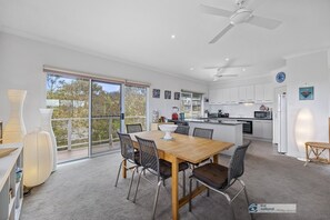 Enjoy meals in the dining area with a wooden table and four chairs, surrounded by large windows offering a view of the outdoors.