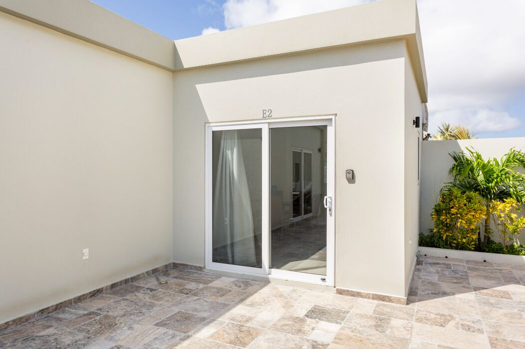 A building with a sliding glass door marked "E2," a tiled patio, and some greenery.