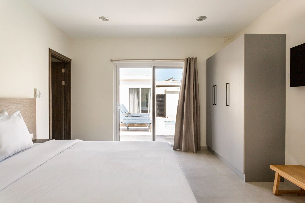 Una camera d'albergo con un letto, una panca, una TV e una porta-finestra scorrevole che dà su un balcone con una sedia.