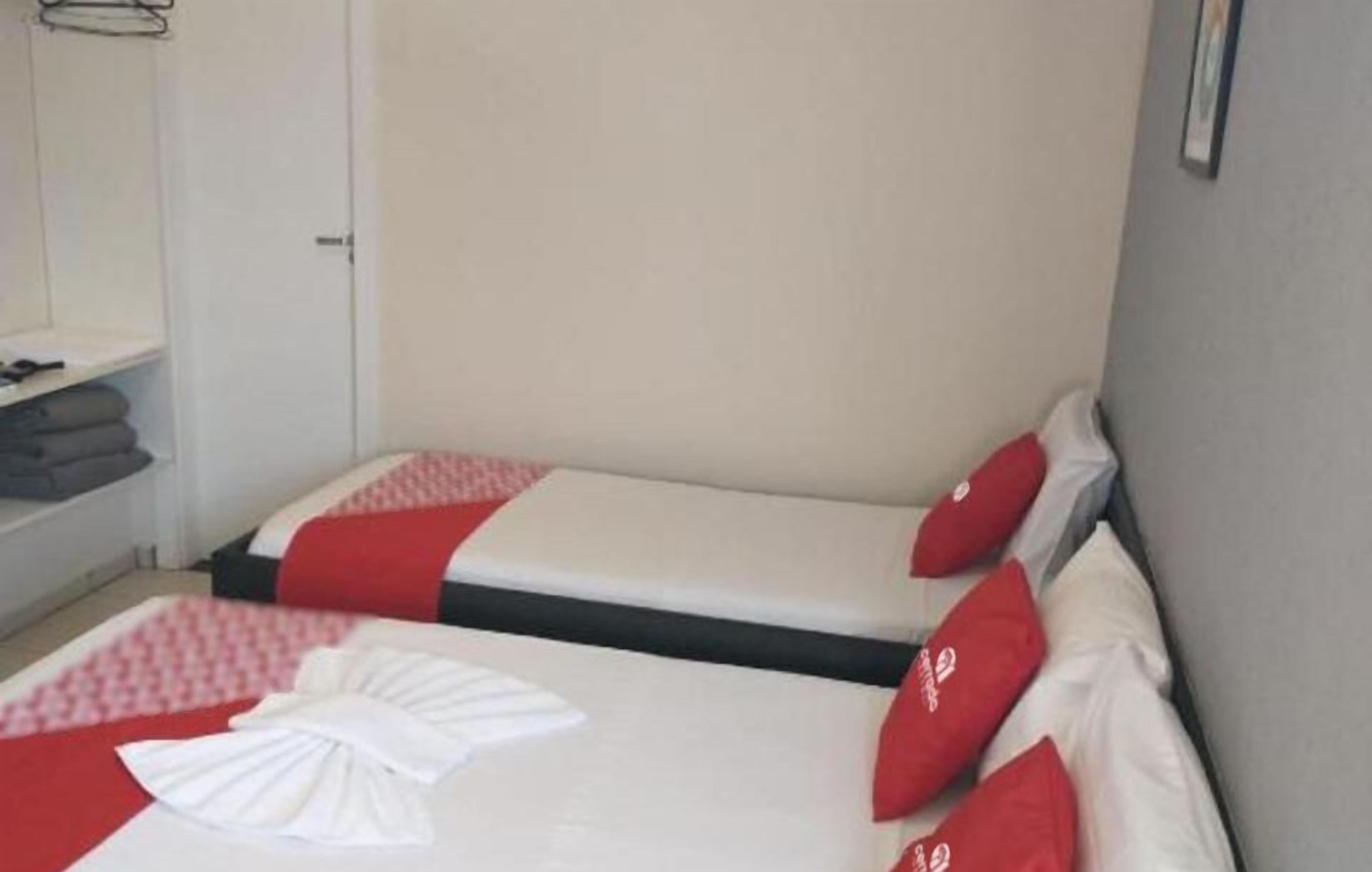 Une chambre d’hôtel avec deux lits, chacun agrémenté de draps rouges et blancs, et un lit parfaitement fait avec une serviette blanche.