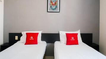 Habitación de hotel con dos camas, cada una con un almohadón rojo y una colcha blanca. En la pared, sobre las camas, hay una obra de arte enmarcada.