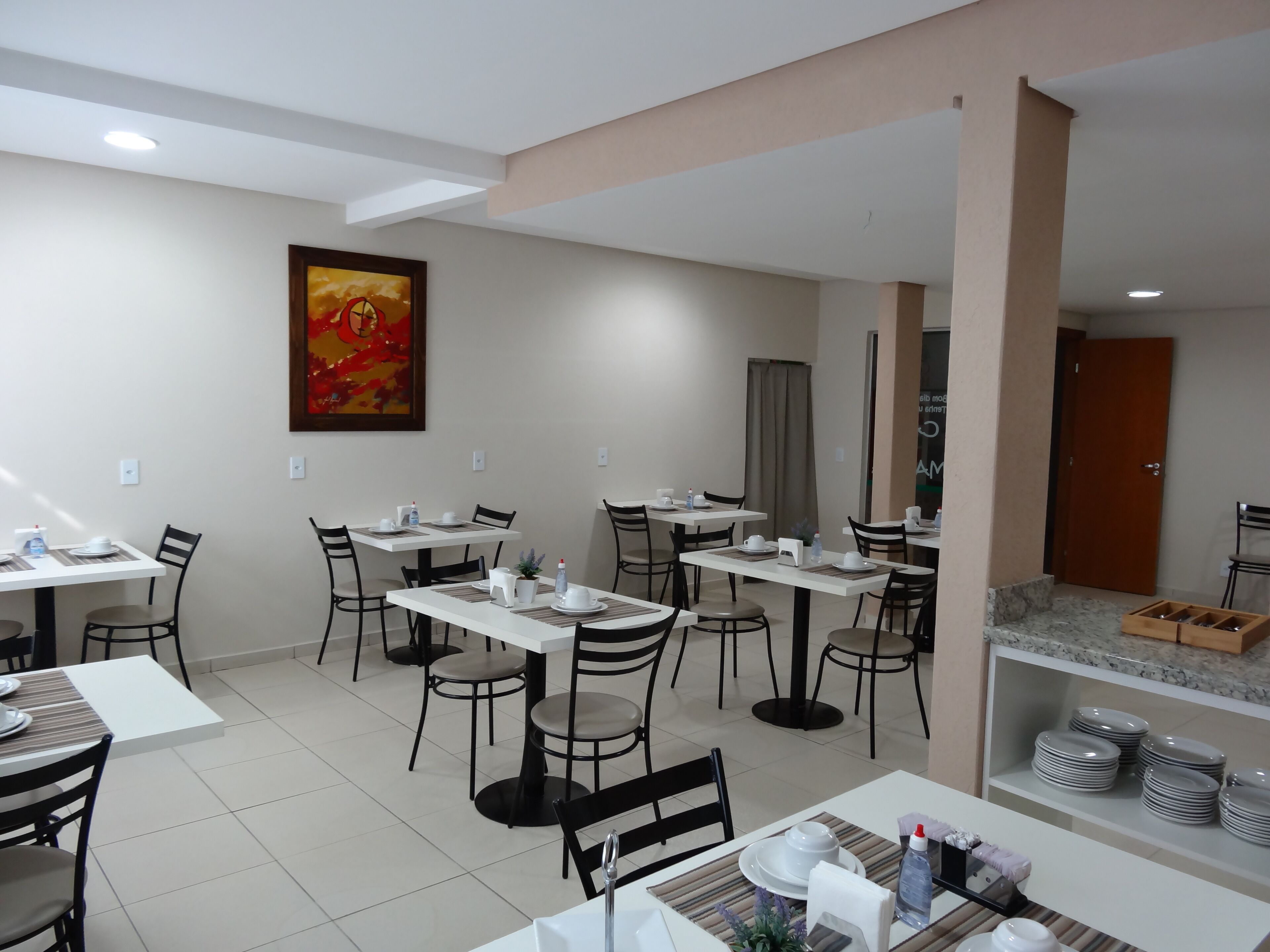 Un espace repas moderne avec plusieurs tables et chaises, un tableau au mur et une porte donnant sur une autre pièce.