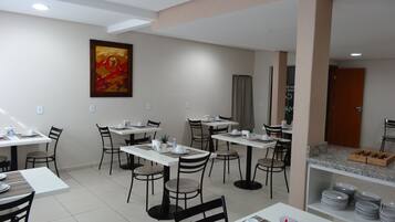 Un espace repas moderne avec plusieurs tables et chaises, un tableau au mur et une porte donnant sur une autre pièce.
