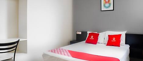 A hotel room with a bed, a desk, and a chair. There are two red pillows on the bed.