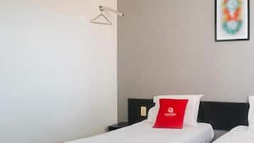 Habitación de hotel con dos camas, almohada roja con un logo, cuadro abstracto enmarco y unidad de aire acondicionado.