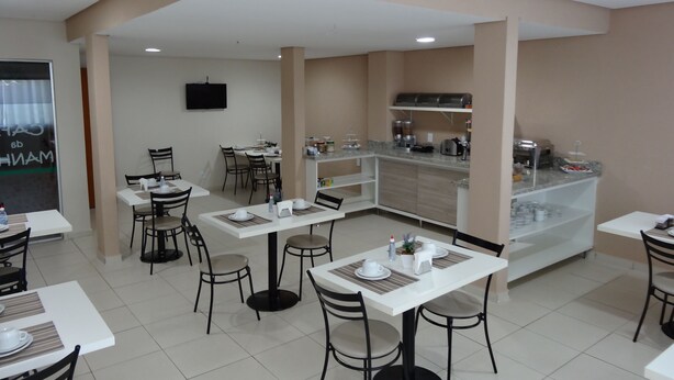 A modern dining area with white tables and chairs, a kitchen counter with appliances, and a TV mounted on the wall. - Cerrado Hotel (Campo Grande)