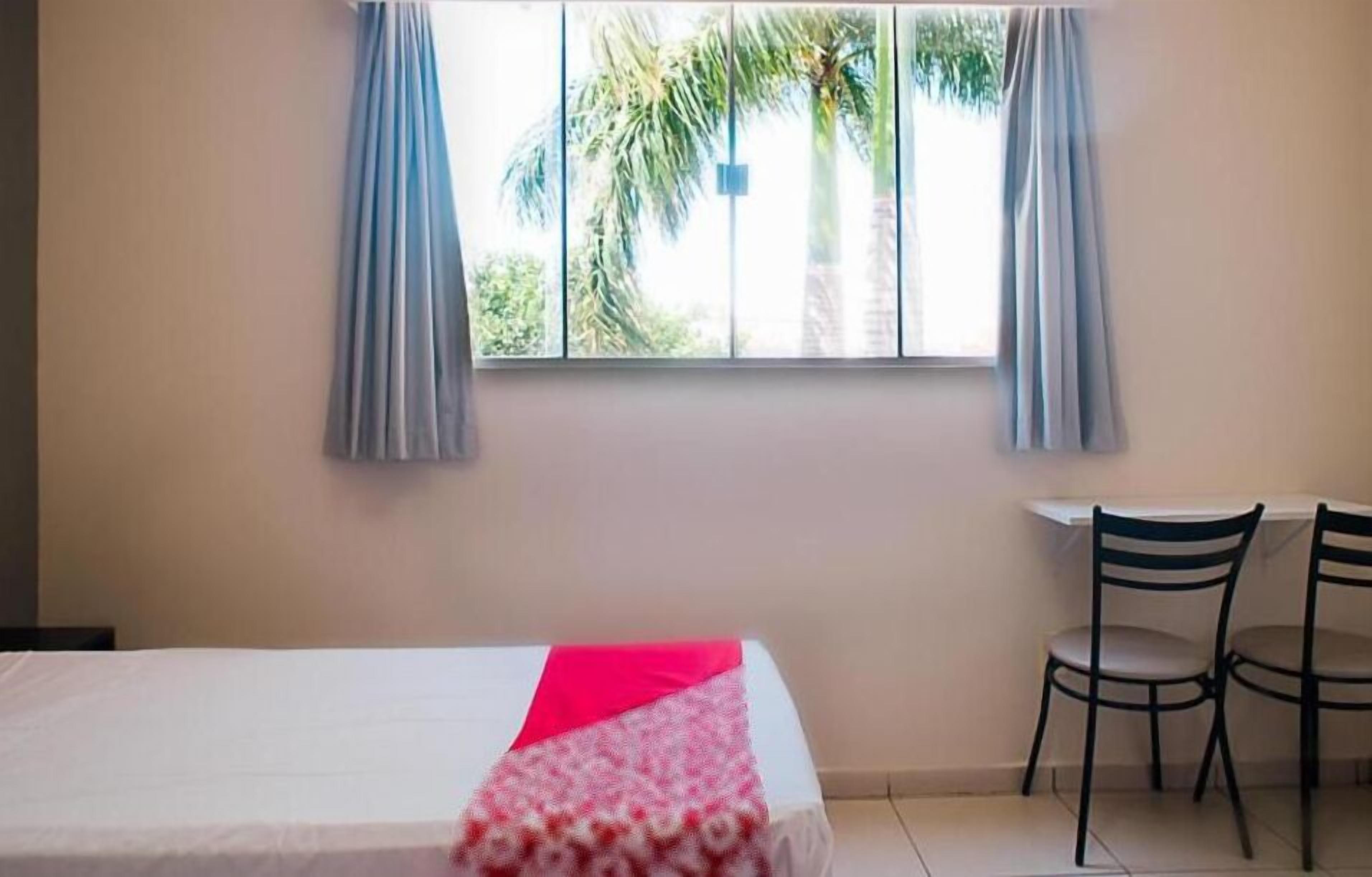 Una habitación con una cama, dos sillas, una ventana con cortinas y vistas a palmeras.