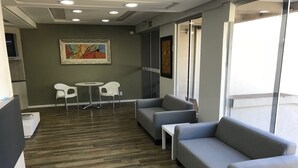 A modern office space with grey sofas, a white table, and a painting on the wall. - Cerrado Hotel (Campo Grande)