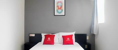A hotel room with a bed, two pillows, a nightstand, a framed picture on the wall, and a window with curtains.