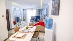 A modern living room with a dining area, a large water dispenser, and a television. - Silver Harbor Kilimani View Palace Apart (Nairobi)