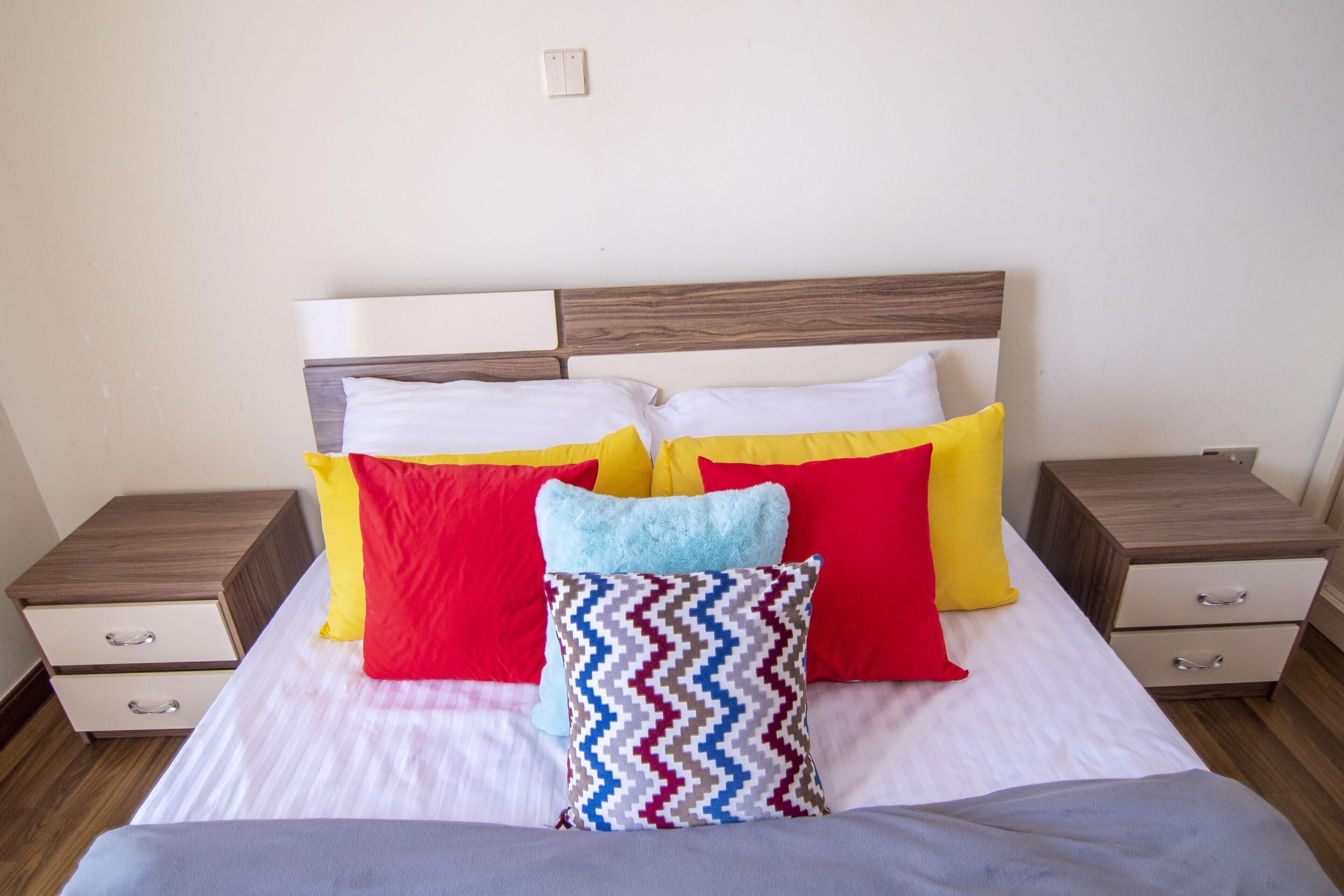 Una cama bien hecha con cabecera de madera, dos mesitas de noche y un pequeño tocador.