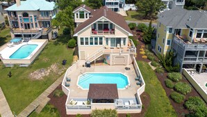Una amplia casa de dos pisos con piscina, terraza techada y varios balcones.