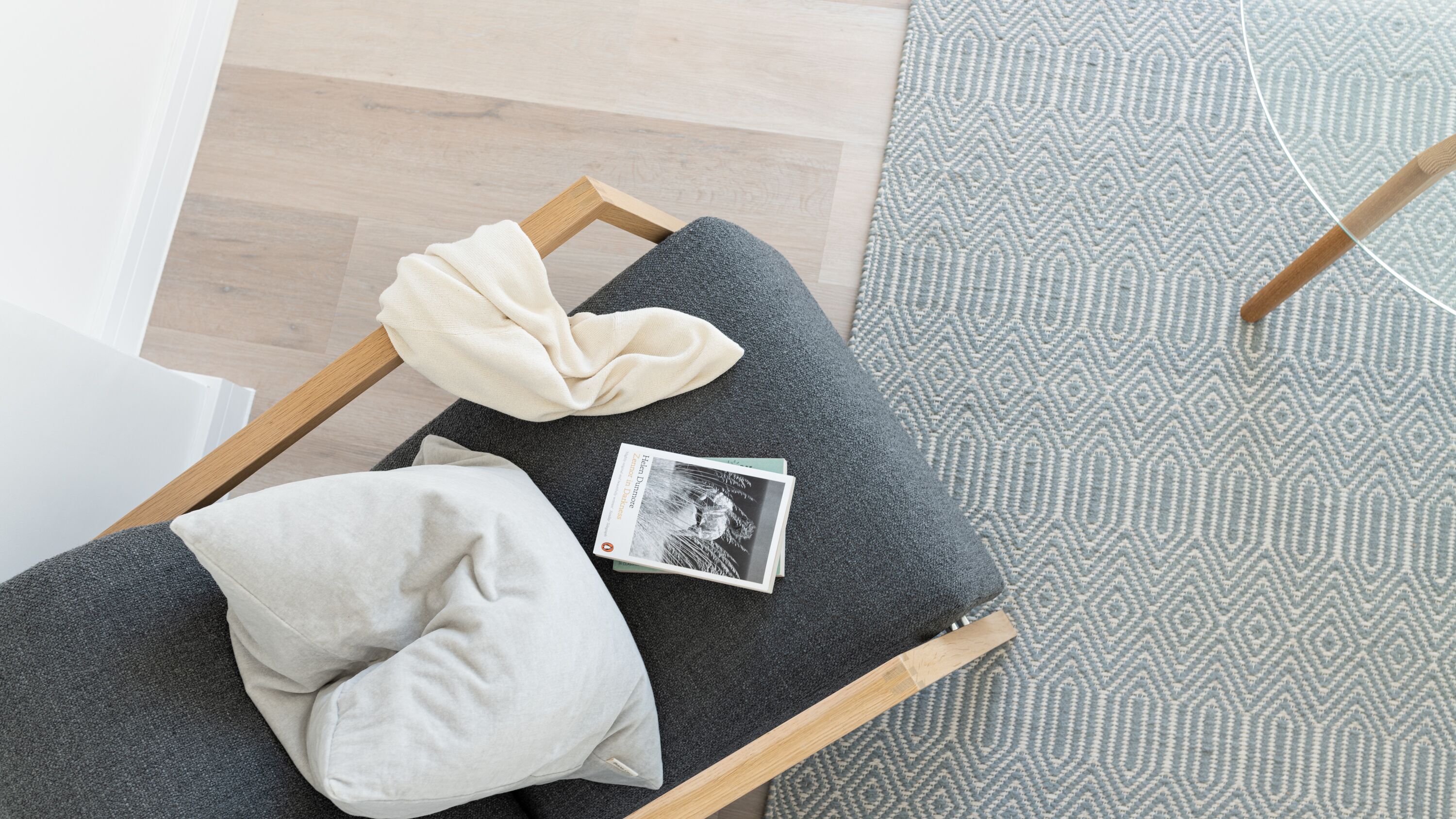 A small, cozy reading nook with a wooden bench, a grey cushion, a white pillow, and a book.