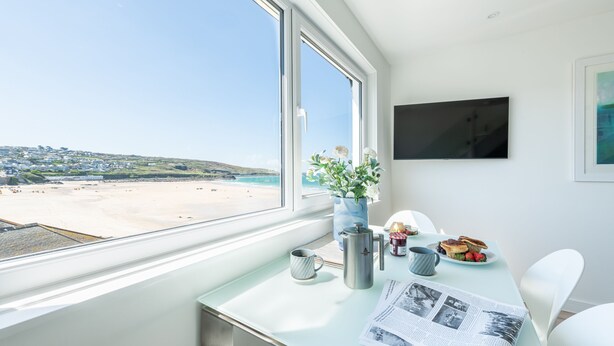 Una stanza con un'ampia finestra vista spiaggia, un tavolo con prodotti per la colazione, una caffettiera e un giornale.