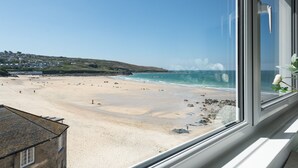 Una spiaggia con vista sull'oceano attraverso una finestra, un edificio con facciata in pietra e cielo sereno.