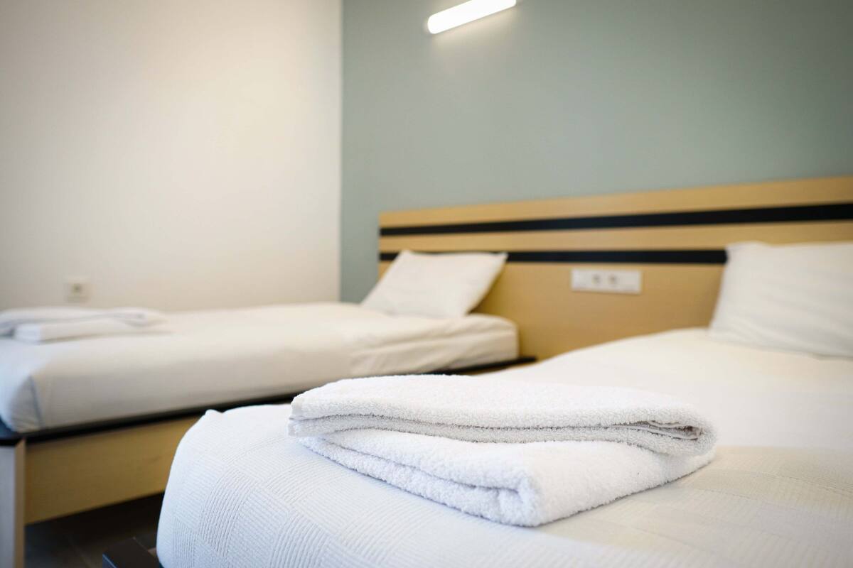 Quarto de hotel com duas camas, cada uma com toalhas brancas bem dobradas e cabeceira de madeira.