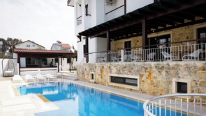 A swimming pool with a stone wall and a covered area with chairs. - Villa Hania (Manavgat)