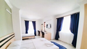 A hotel room with a large bed, a desk with a chair, a TV, and two windows with curtains. - Villa Hania (Manavgat)