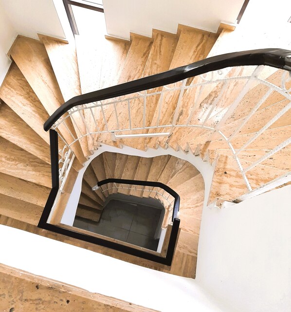 A spiral staircase with wooden steps and a black handrail, leading to an upper floor.