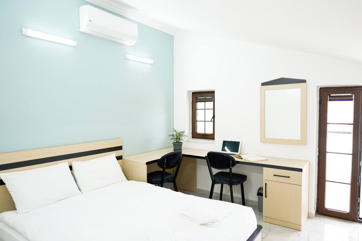 Quarto com cama, escrivaninha, duas cadeiras, computador e um pequeno armário.