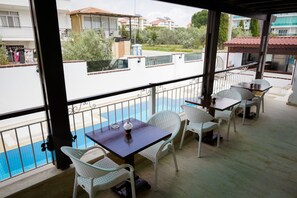 A balcony with white wicker chairs and a table, overlooking a swimming pool and residential buildings. - Villa Hania (Manavgat)
