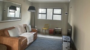 A living room with a brown leather sofa, a small table, a chair, a floor lamp, and a TV stand. - Exquisite one bedroomed apartment - 2043 (Bulawayo)