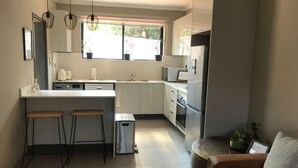 A modern kitchen with white cabinets, a central island with stools, a sink, and a refrigerator. - Exquisite one bedroomed apartment - 2043 (Bulawayo)