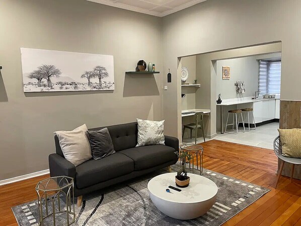 A modern living room with a black sofa, a round coffee table, and a painting of trees on the wall.