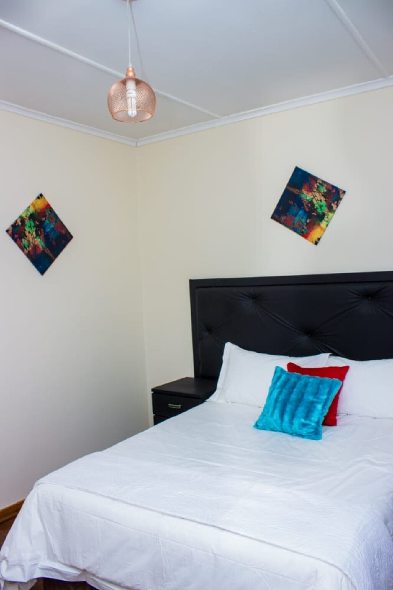 A neatly made bed with white linens and a single blue pillow, a black headboard, and a small bedside table with a lamp.