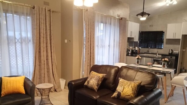 Una sala de estar moderna con un sofá de cuero negro, una mesita de centro redonda y un comedor con una cocina al fondo.