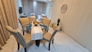 Un comedor con una mesa redonda de cristal, cuatro sillas y un centro de mesa decorativo.