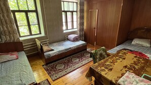 Une chambre avec deux lits, une armoire en bois, un ventilateur de plafond et une fenêtre avec des rideaux.