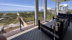A balcony with a view of the ocean, a wooden deck, and a seating area with cushions.