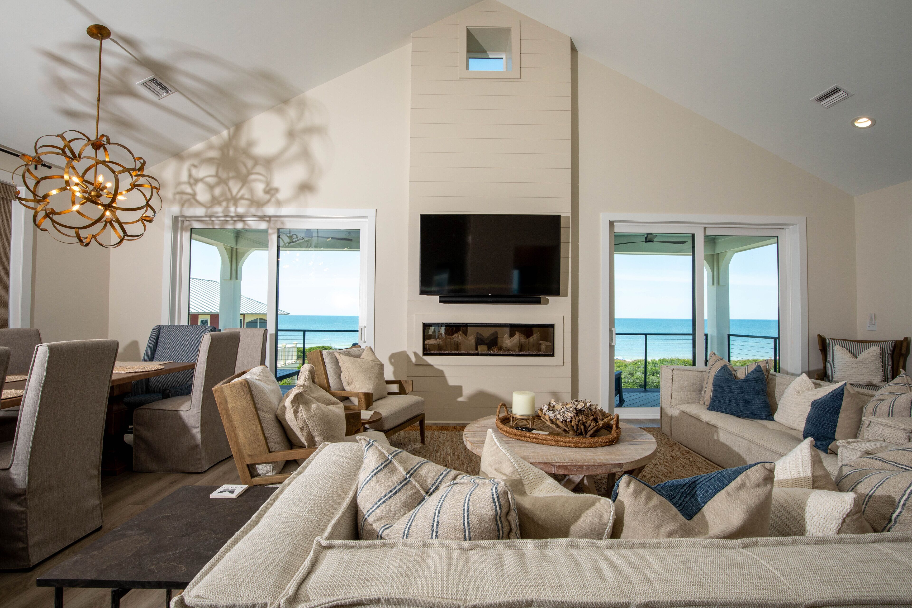 A spacious living room with a large TV, comfortable seating, and a view of the ocean.