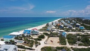 An aerial view of a coastal residential area with houses, a beach, and a clear blue sky.