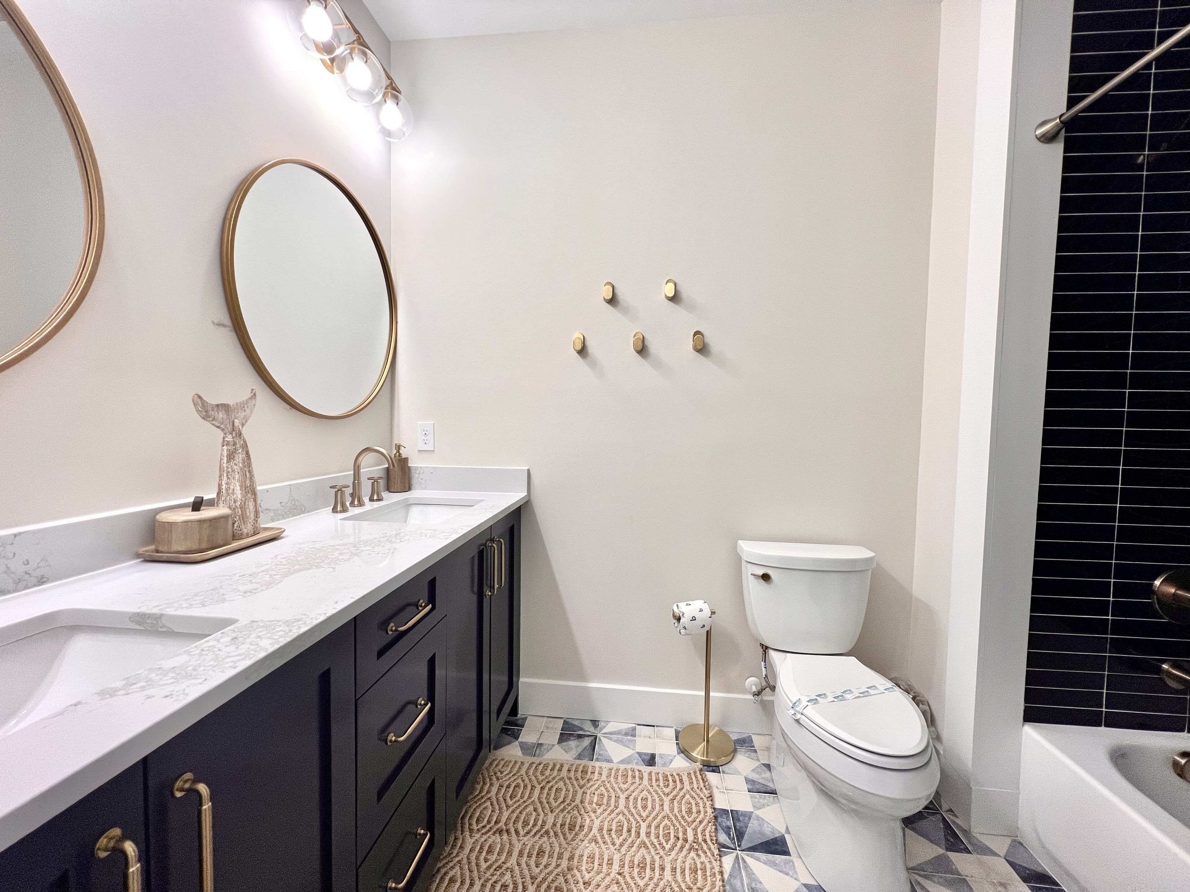 A bathroom with a white toilet, a sink with a marble countertop, dark cabinets, and a patterned rug.