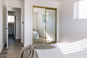A bedroom with a bed, a large mirror, a wardrobe, and a view of a kitchen.