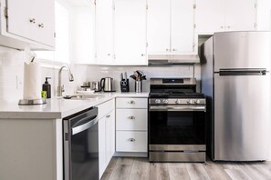 A modern kitchen with white cabinets, stainless steel appliances, and a wooden floor. - The Cozy Crib / Spacious & Workspace w/ Monitor (Salt Lake City)