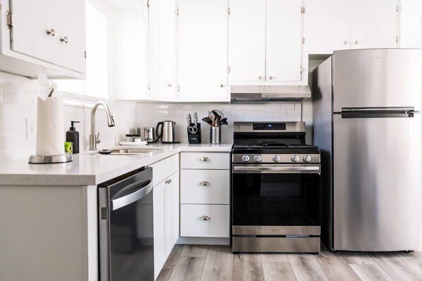 A modern kitchen with white cabinets, stainless steel appliances, and a wooden floor.