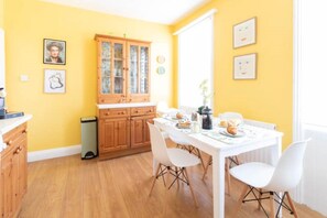 Un comedor luminoso de color amarillo con un aparador de madera, sillas blancas y una mesa preparada para el desayuno.