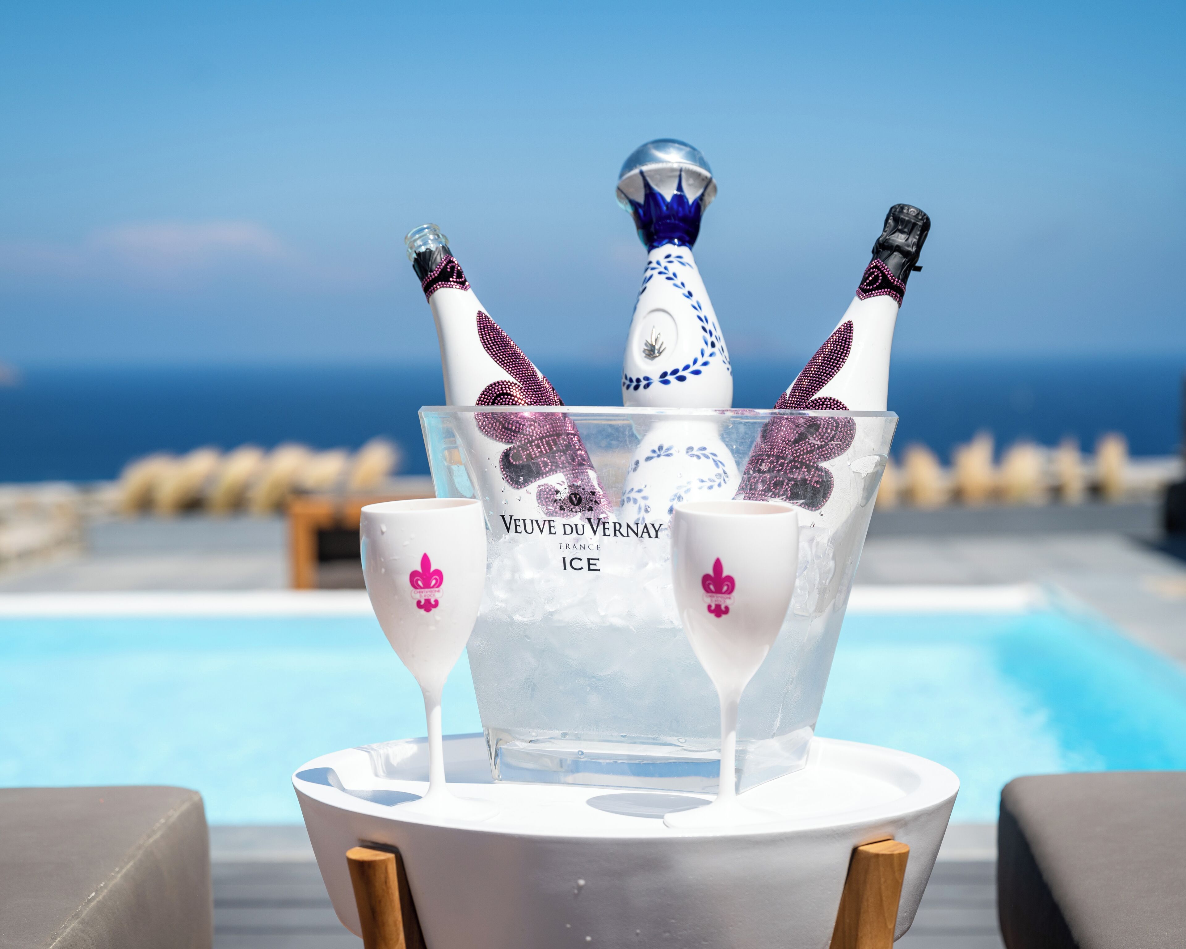 A poolside setting with a champagne bucket containing bottles and glasses, and a pool in the background.