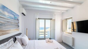 A hotel room with a bed, a painting, a television, and a view of the sea through the open door. - Luxury Villa Agavi Ideal for Events (Mykonos)