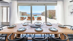 A dining area with a wooden table set for six, overlooking a pool and stone walls. - Luxury Villa Agavi Ideal for Events (Mykonos)