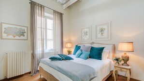 Una camera da letto con un letto grande, due comodini con lampade, un termosifone e una finestra con tende.