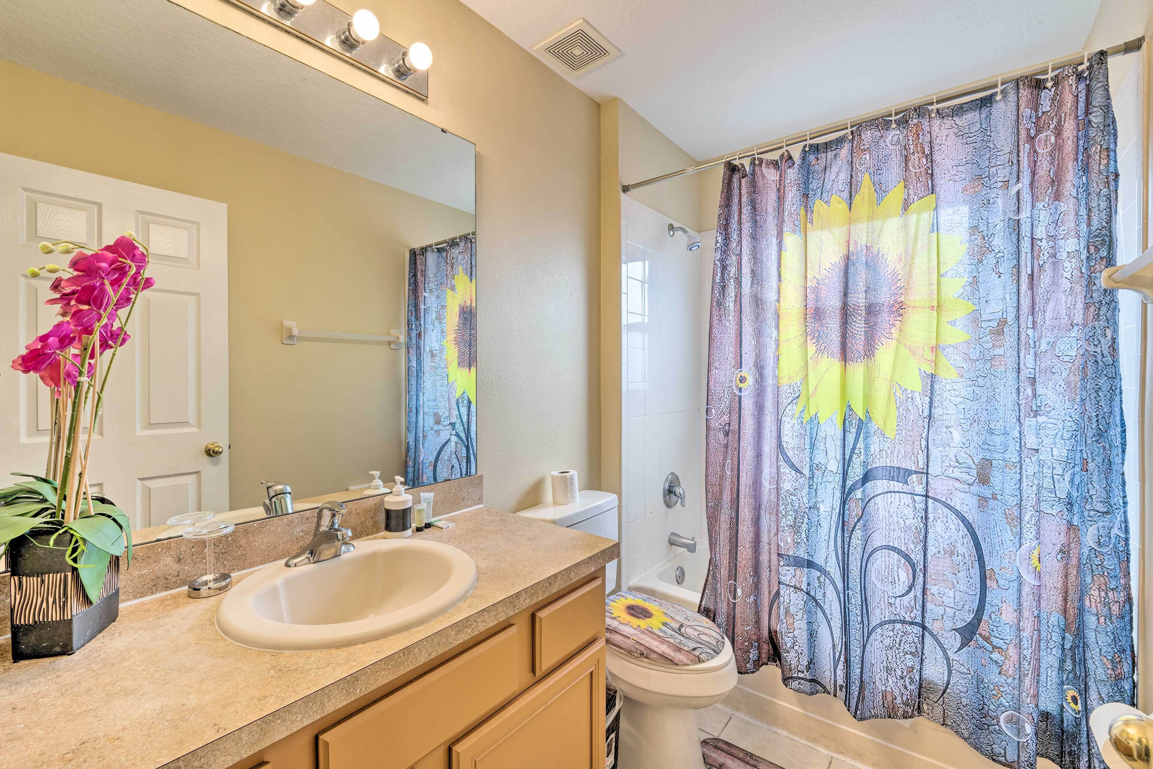 A bathroom with a sink, mirror, toilet, and shower curtain with a sunflower design.