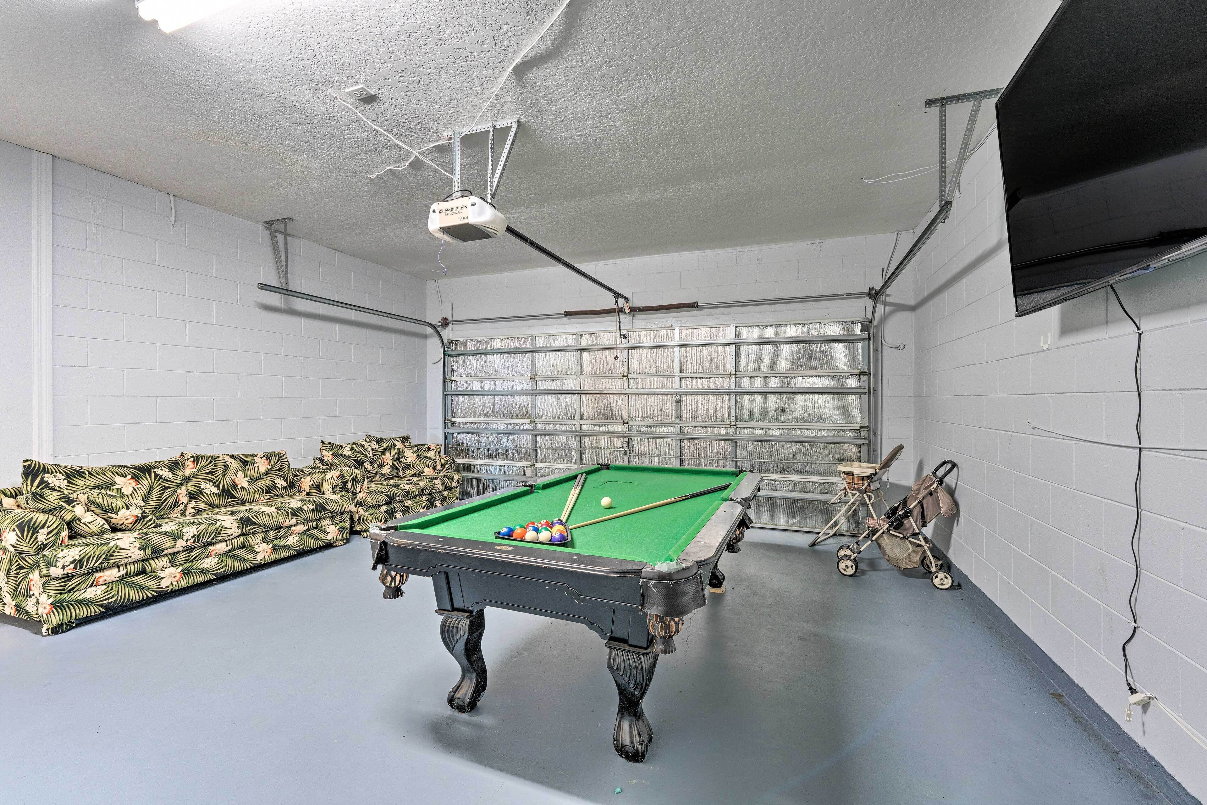 A pool table in a room with white brick walls, a ceiling fan, and a television mounted on the wall.
